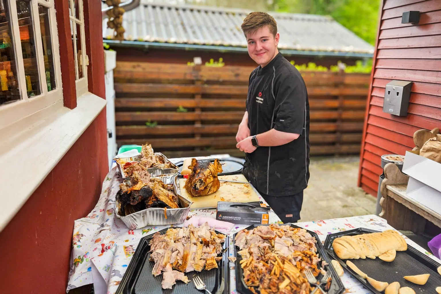 Kok ved udskæringsbordet med helstegt pattegris, udskåret kød og brød klar til servering